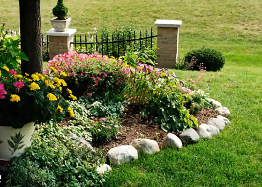 A tidy backyard with mulched beds, a small lawn area, and stone edging separating planting beds from grass.