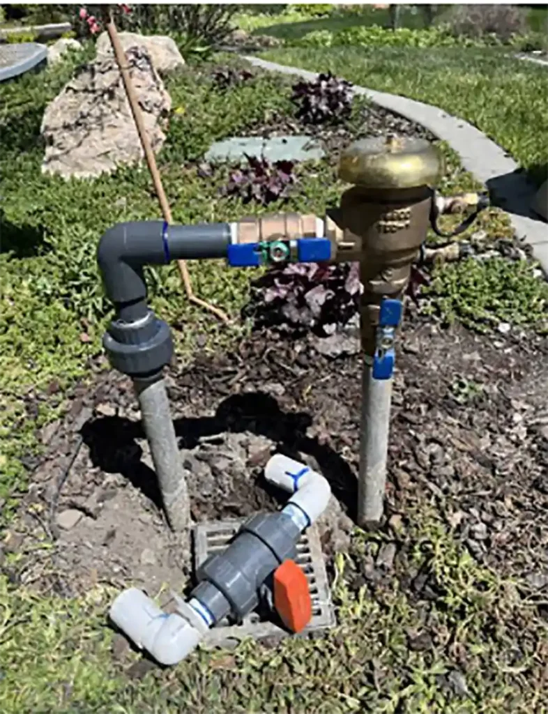 Brass backflow preventer assembly mounted on an outdoor pipe beside a house wall