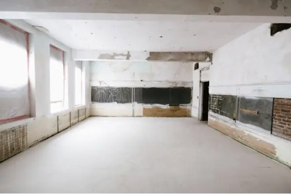 Renovation tools, a ladder, and building materials on the bare floor of an empty room under repair