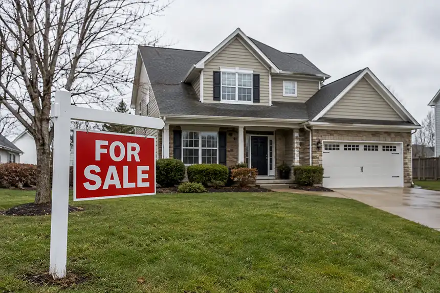 For sale sign in the front yard of a suburban house on an overcast day