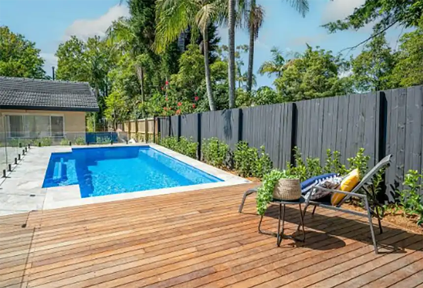 Residential backyard pool with surrounding planting, walking space, safety fencing, and accessible pool equipment area.