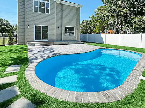 Completed fiberglass swimming pool with a finished patio and landscaped backyard.