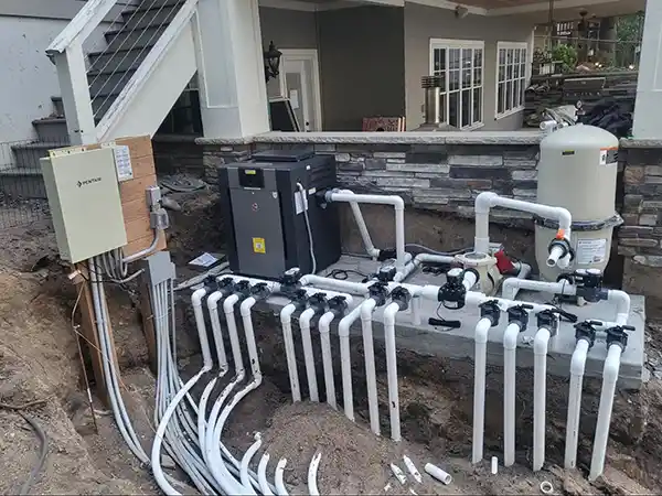 PVC plumbing lines connecting an in-ground fiberglass pool to its filtration equipment.